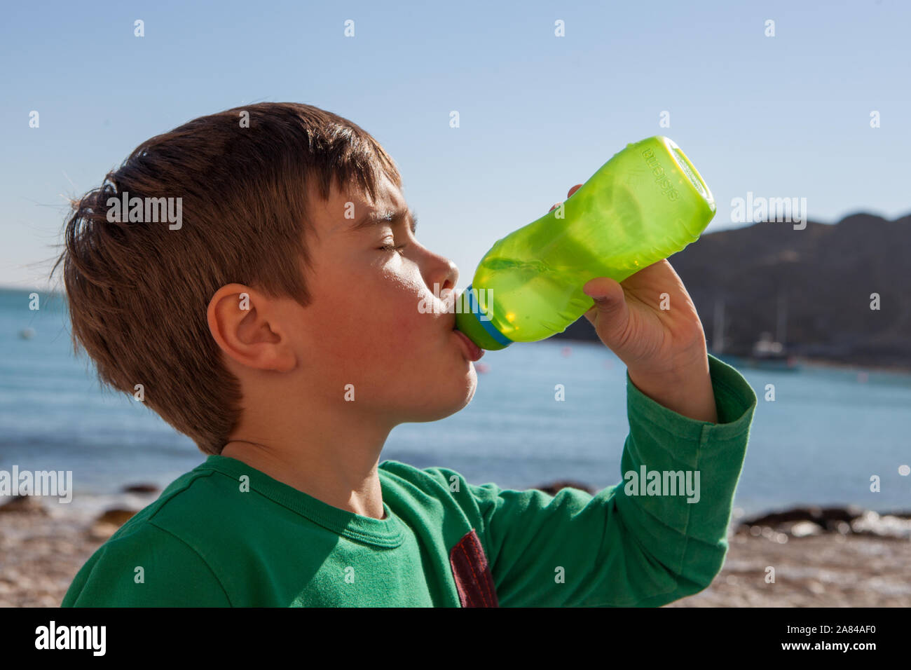 Ein kleiner Junge trinkt Wasser aus einer Wasserflasche an einem heißen Sommertag am Strand, England. Stockfoto