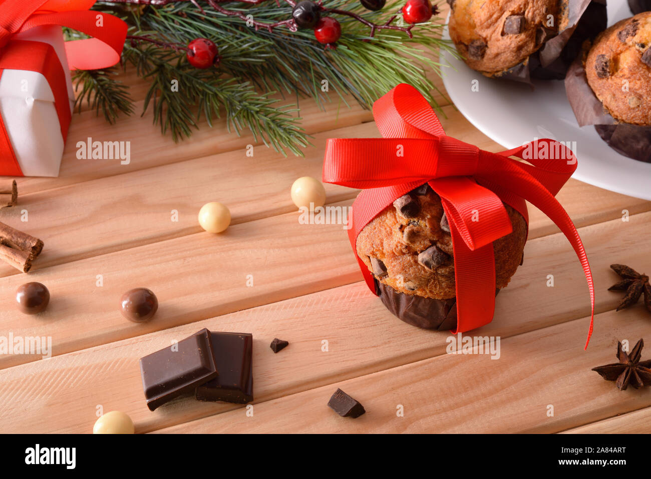 Chocolate Chip muffin auf Holztisch mit Weihnachten Objekte mit roten Schleifchen verziert. Horizontale Komposition. Erhöhte anzeigen. Stockfoto