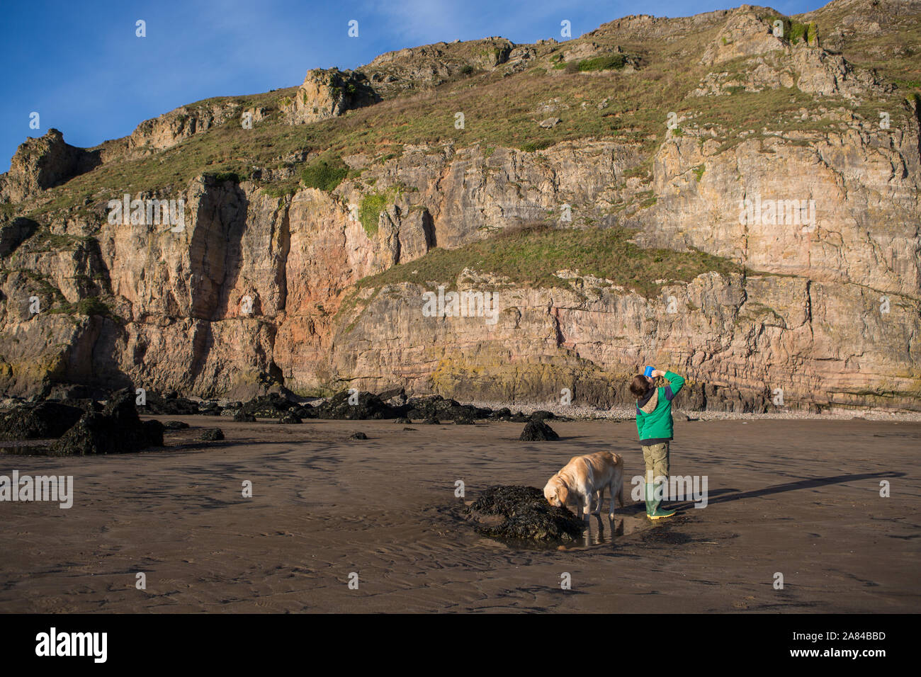 Ein kleiner Junge, der heiße Schokolade an einem leeren Strand in Großbritannien trinkt Stockfoto