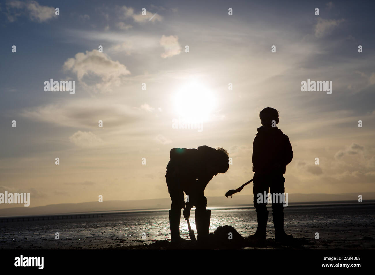 Eine Silhouette von zwei Jungen graben und Sandburgen am Strand im Winter, Großbritannien Stockfoto