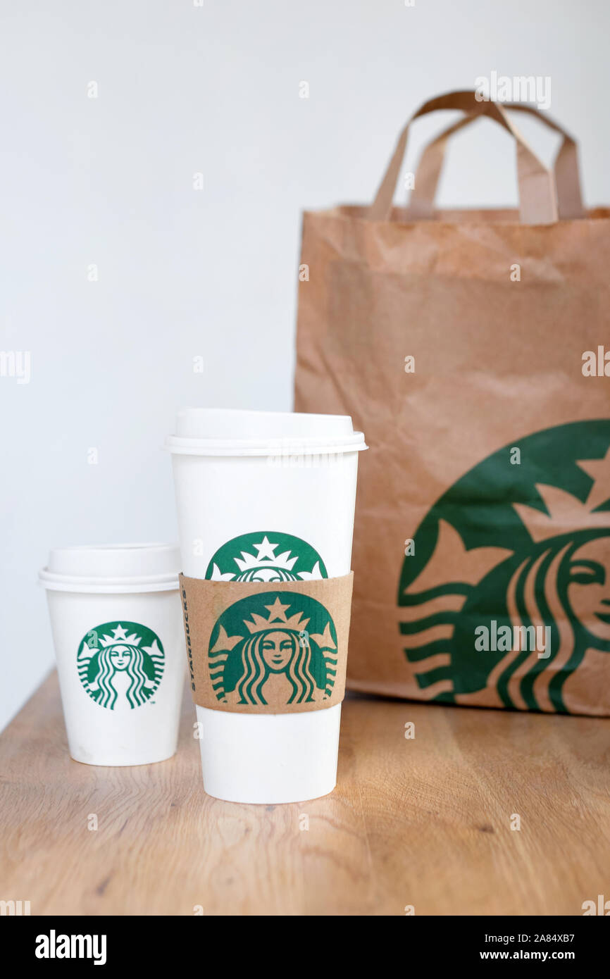 Kiew, Ukraine/November 06, 2019: Starbucks Kaffee nehmen Sie Tassen mit papiertüte auf Holz- zähler Tabelle. American global Kaffee und Kaffeehaus Stockfoto