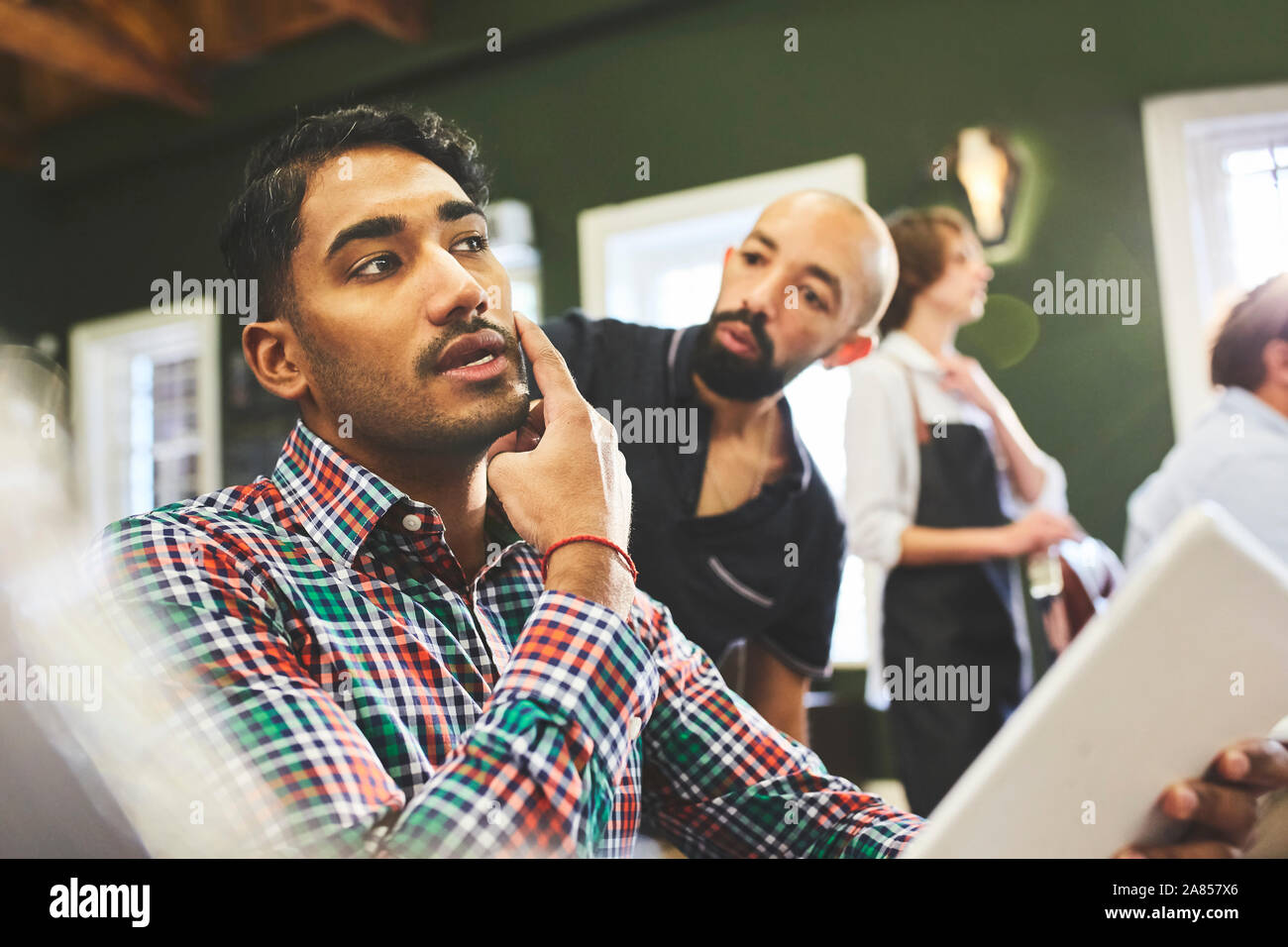 Männliche Kunde und Friseur sprechen in Barbershop Stockfoto