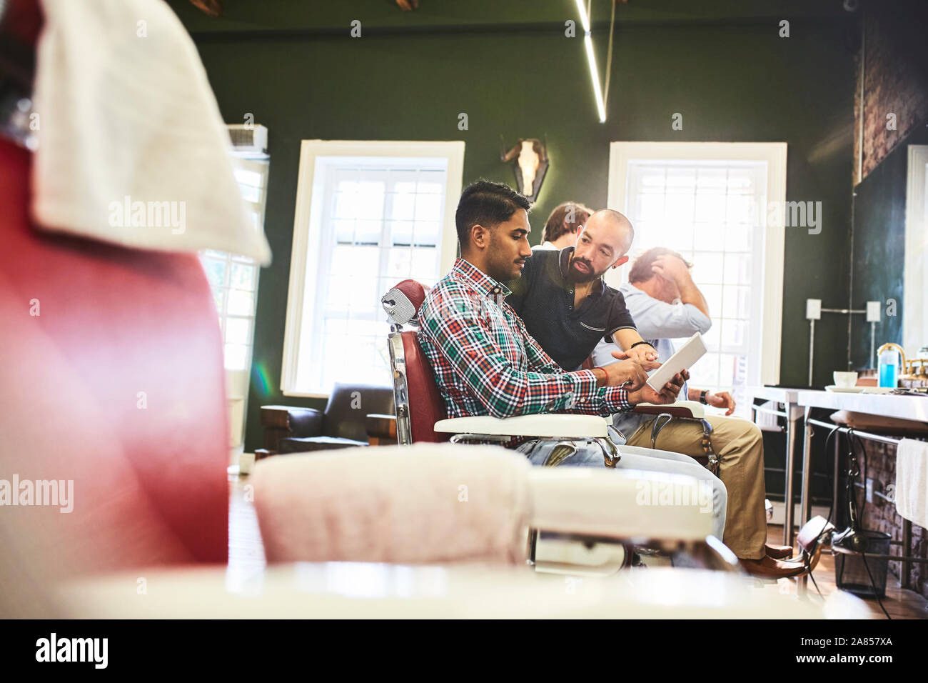 Männliche Friseur- und Kunden mit digitalen Tablet sprechen in Barbershop Stockfoto