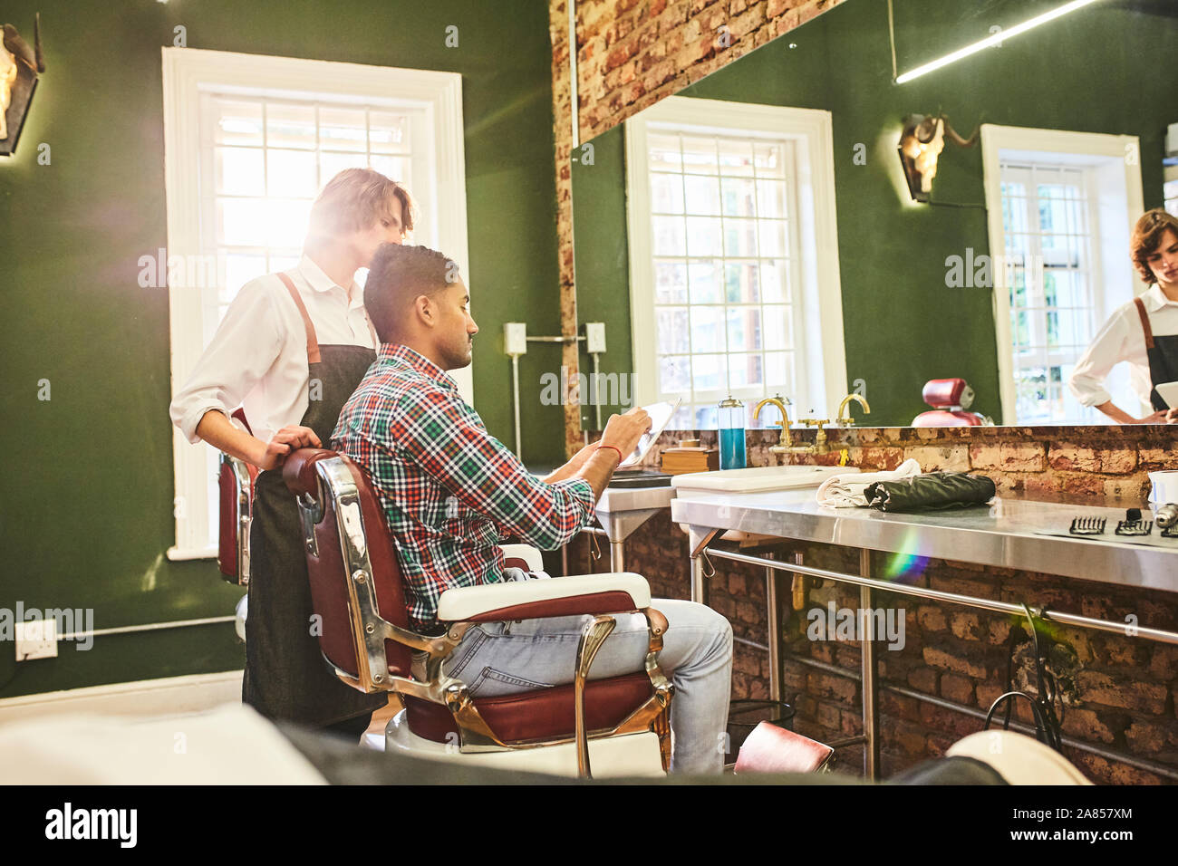 Männliche Friseur- und Kunden mit digitalen Tablet sprechen in Barbershop Stockfoto