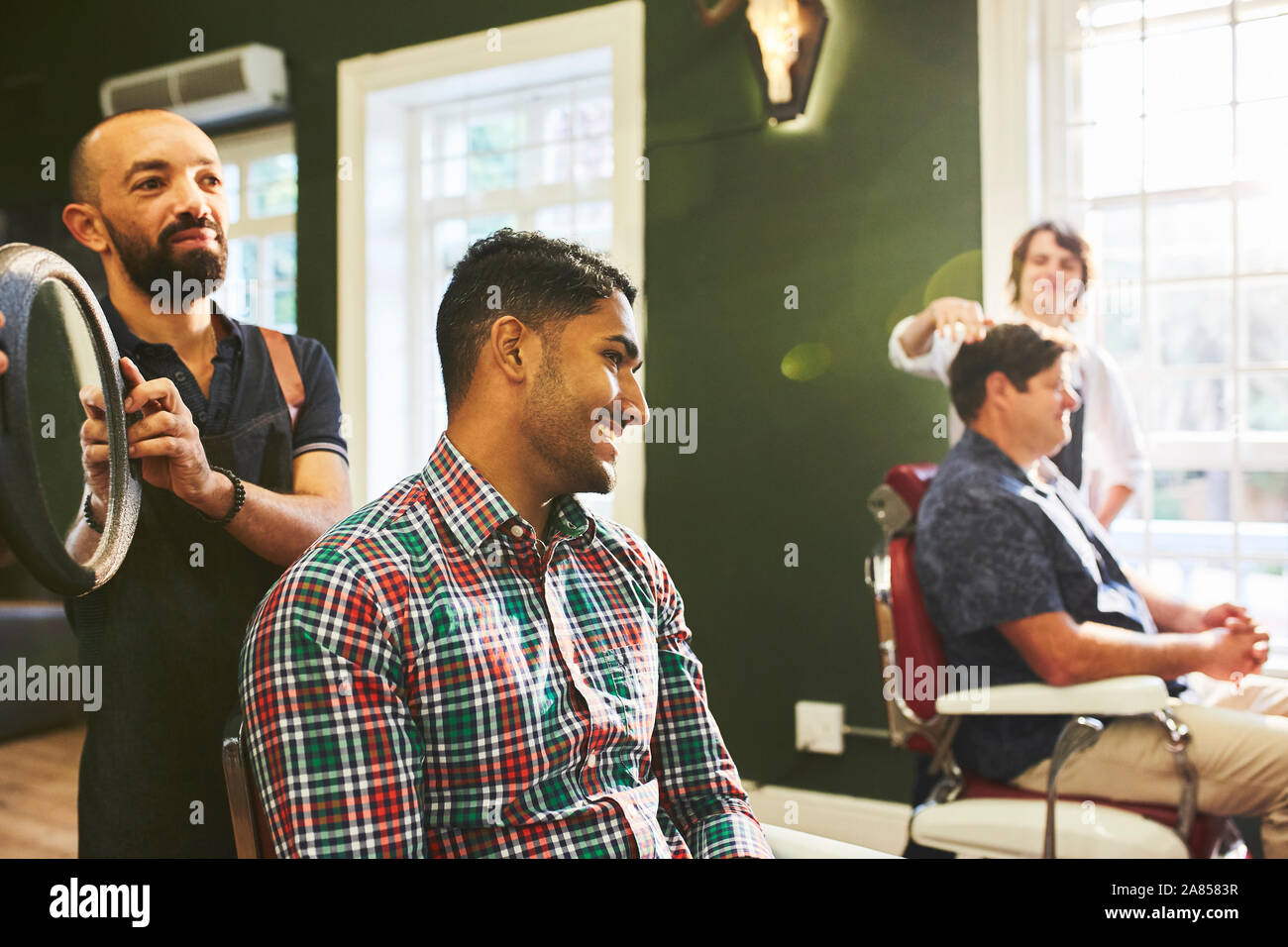 Männliche Friseur mit Spiegel für Lächelnde Kunden im barbershop Stockfoto