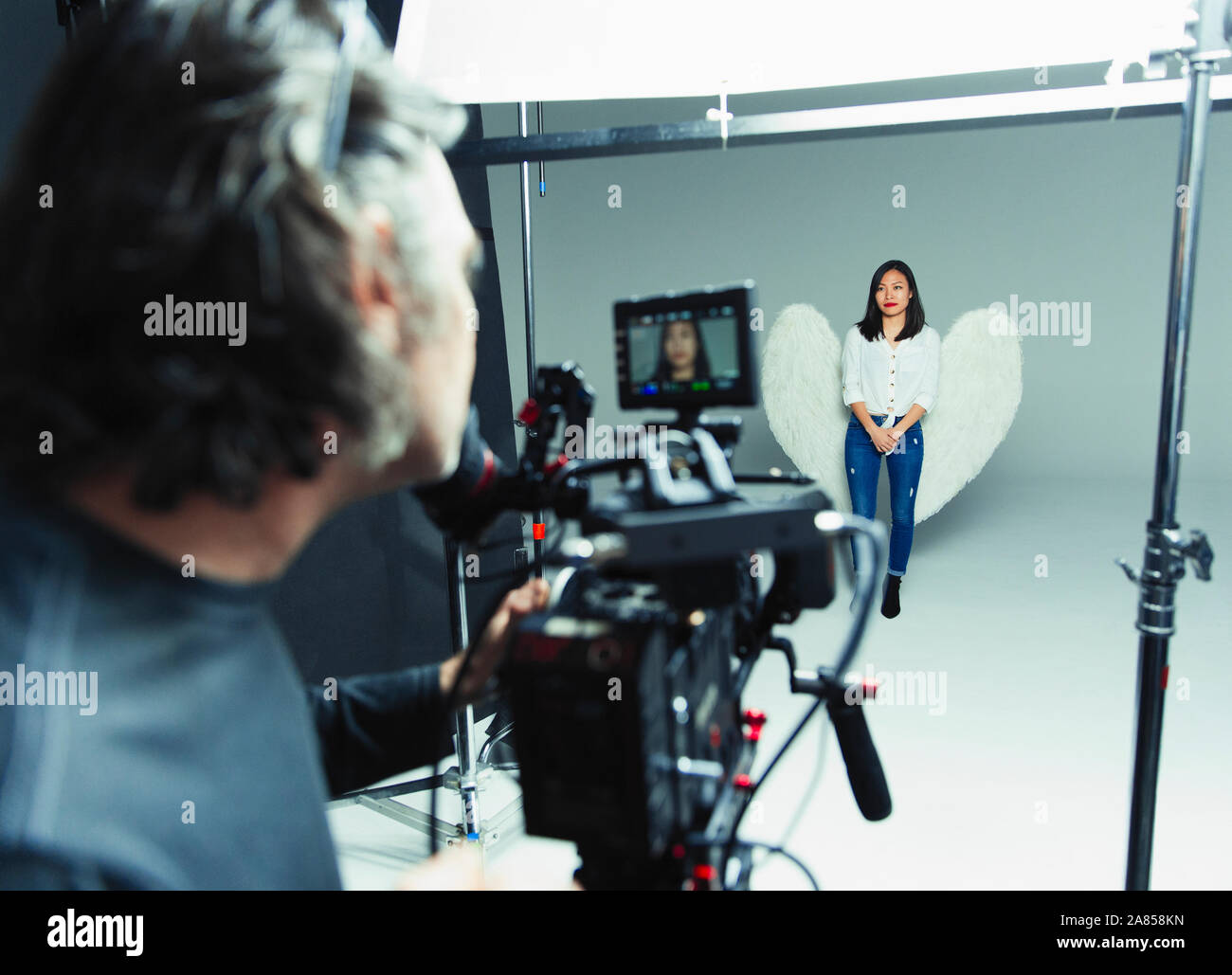 Fotograf hinter der Kamera fotografieren junge Frau trägt Angel Wings beim Fotoshooting im Studio Stockfoto