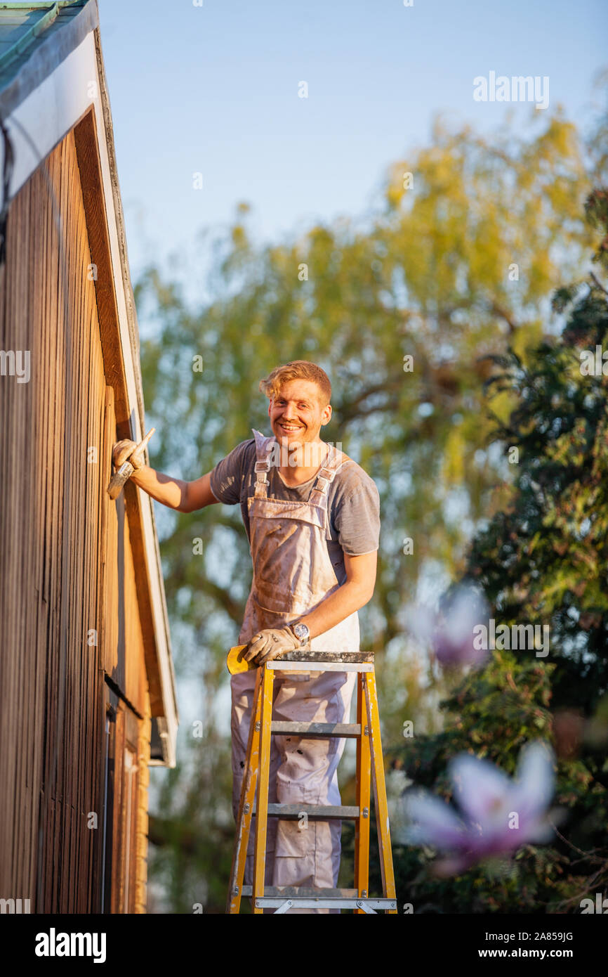 Portrait zuversichtlich männlicher Maler auf der Leiter lackieren home Exterieur Stockfoto
