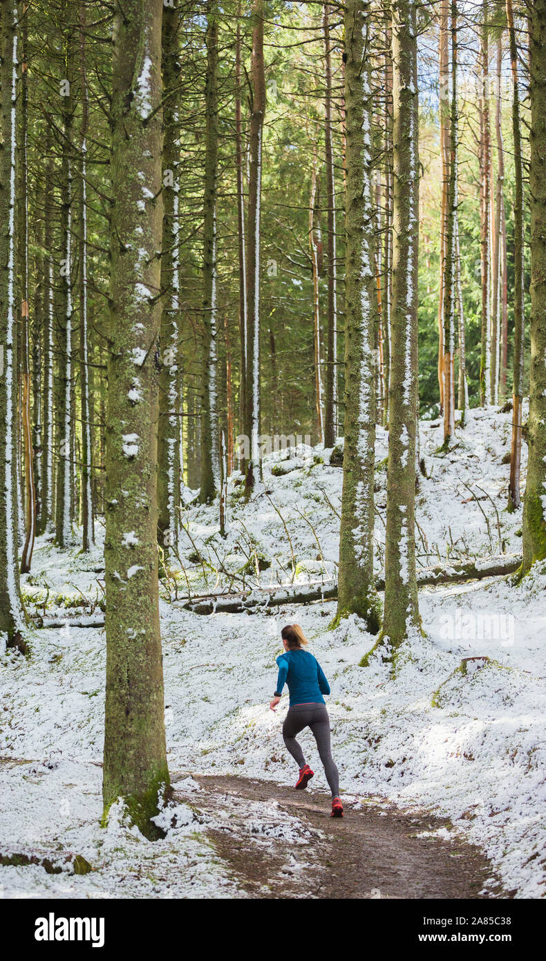 Frau joggen auf verschneiten Pfad im Wald Stockfoto