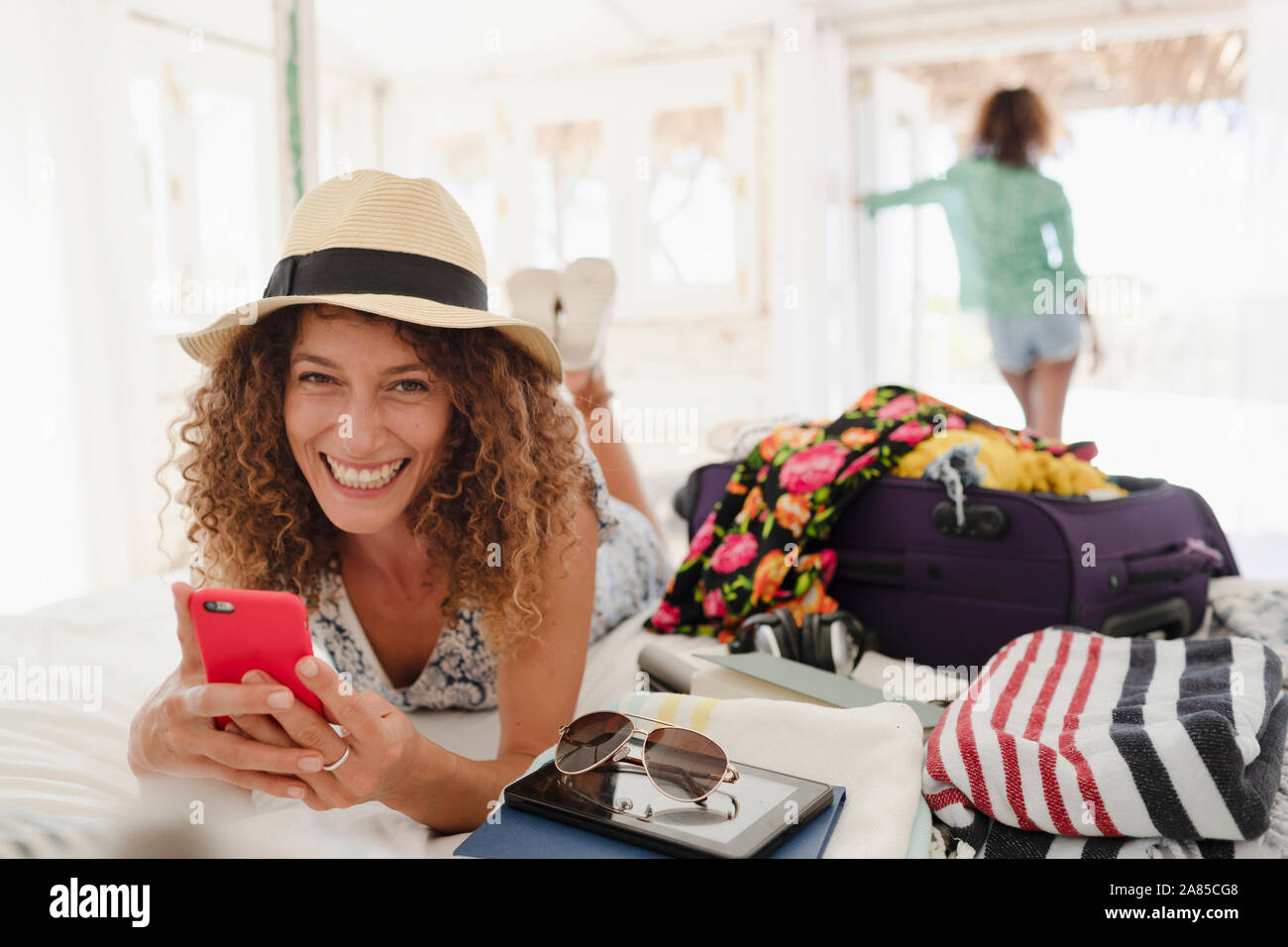Portrait glückliche junge Frau mit Smart Phone, auspacken Koffer im Schlafzimmer Stockfoto