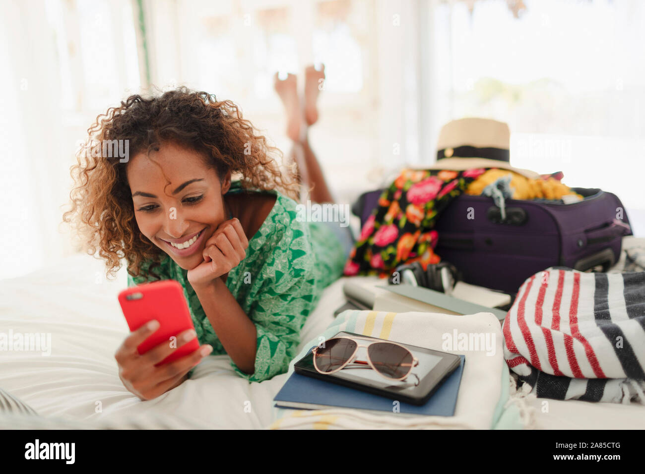 Junge Frau mit smart phone Auspacken der Koffer auf das Bett Stockfoto