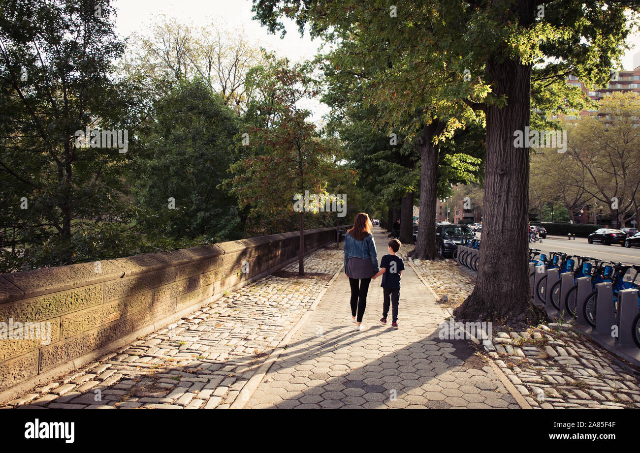 Mutter und Sohn gemeinsam zu Fuß auf dem Bürgersteig von hinten. Stockfoto