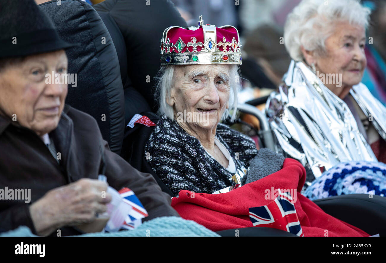 Bewohner von die Royal British Legion Industries Dorf in Kent Winifred Bennett, 101 Jahre alt, trägt ein Spielzeug Krone und ist gegen die Kälte gehüllt, als sie Königin Elisabeth II Anreise Hundertjahrfeier des Nächstenliebe zu feiern erwartet. Stockfoto