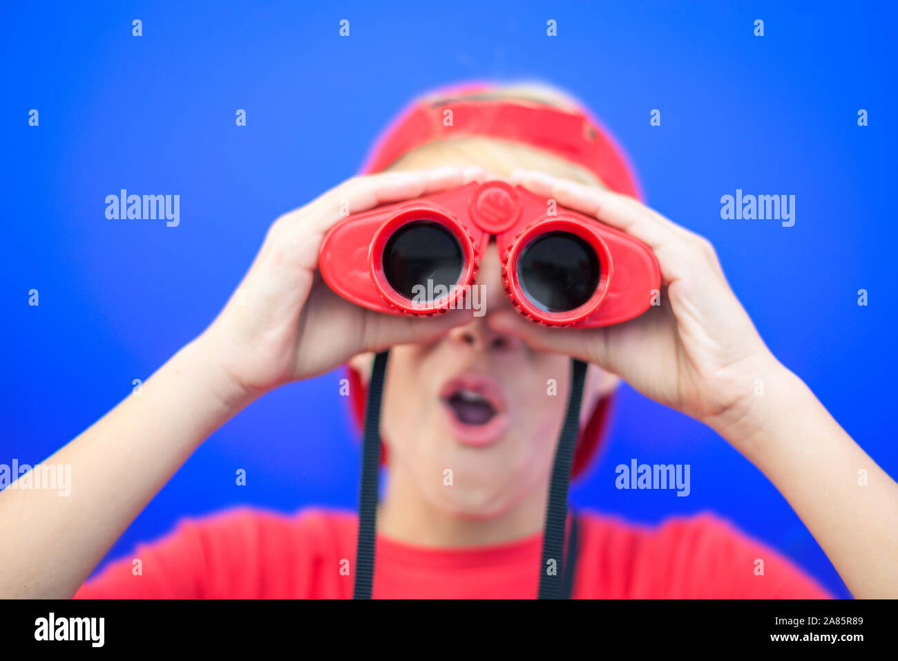 Schöne junge weg schauen mit einem roten Fernglas auf einem blauen Hintergrund. Bunte Bild einer jungen männlichen Spaß mit einem Teleskop. Viel Spaß, Stockfoto
