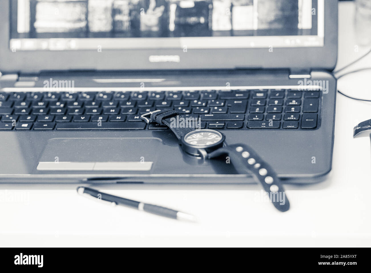 Die Details auf einem Schreibtisch, auf dem ein Laptop, Armbanduhr und Stift ruhen, monochromes Bild. Stockfoto