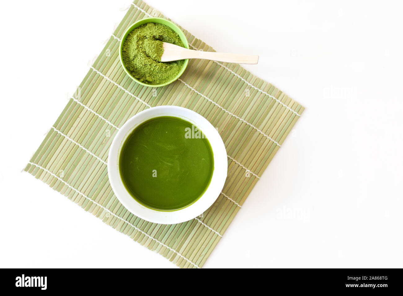 Löffel aus Holz mit pulverisiertem Matcha grüner Tee in der Schüssel, auf weißem Hintergrund. Stockfoto