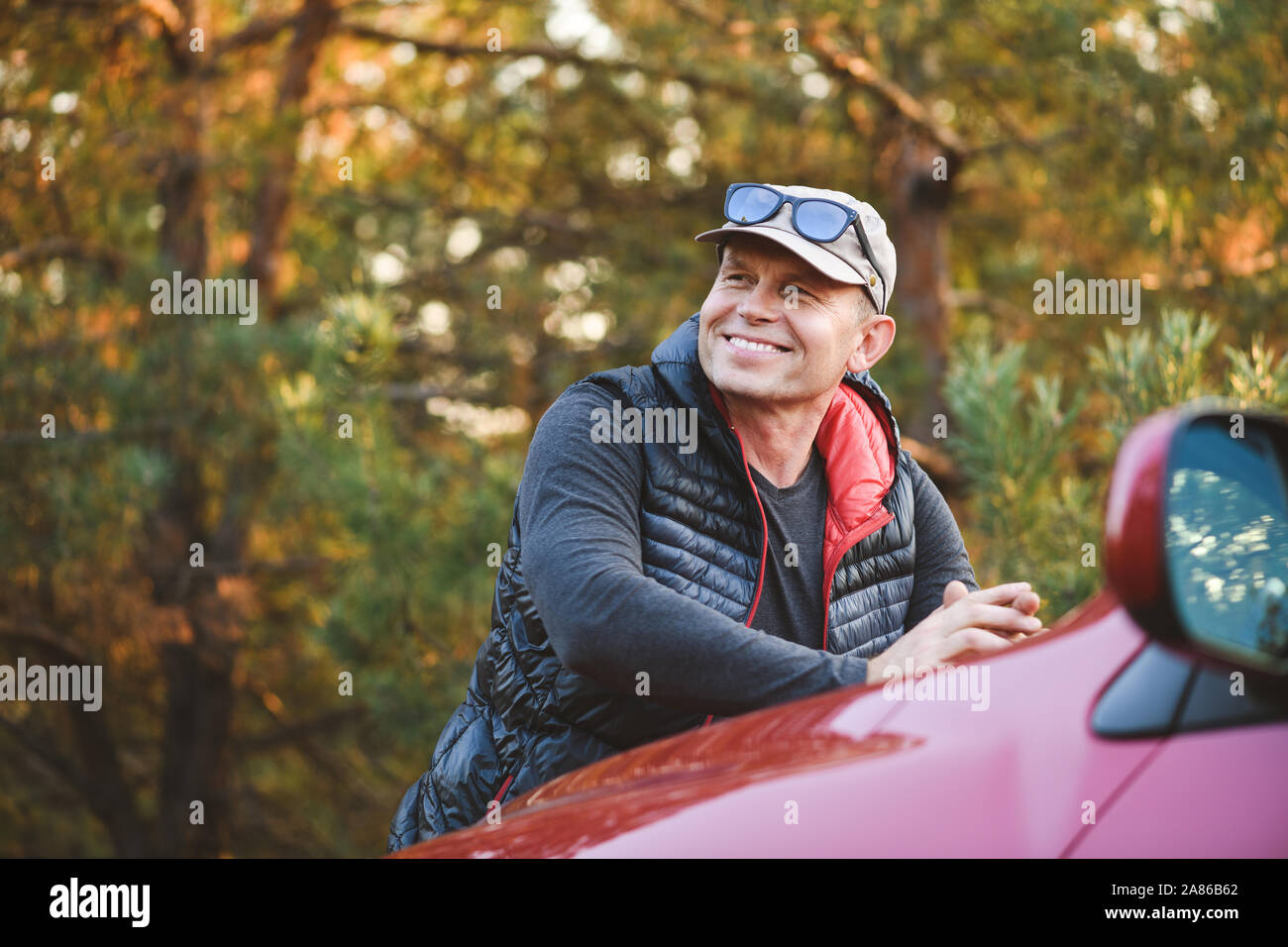 Lächelnd Mann lehnt sich auf der Motorhaube eines Autos. SUV im Wald. Stockfoto