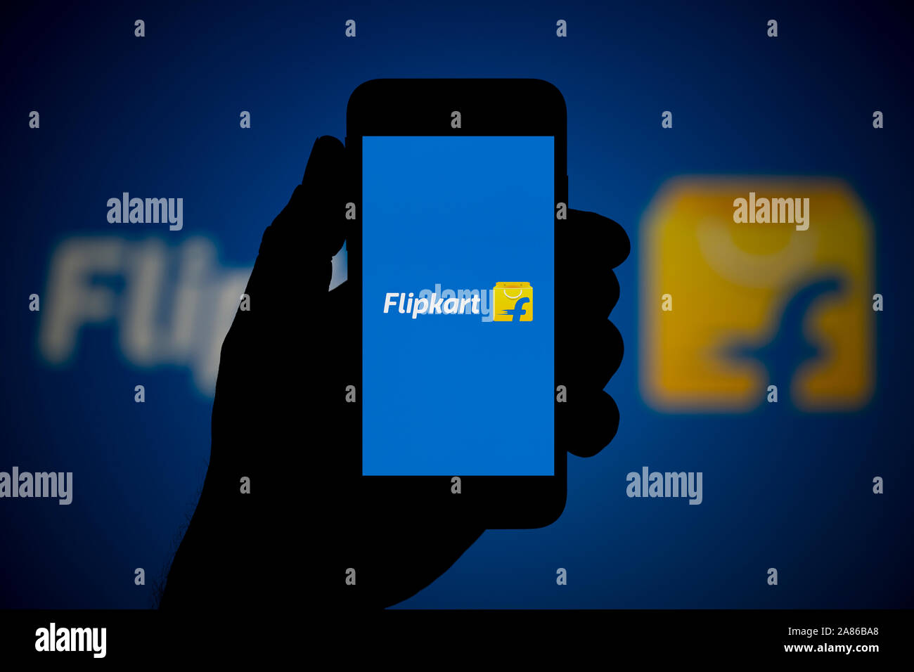 Ein Mann schaut auf seinem iPhone die zeigt die Flipkart Logo, mit dem gleichen Logo im Hintergrund (nur redaktionelle Nutzung). Stockfoto
