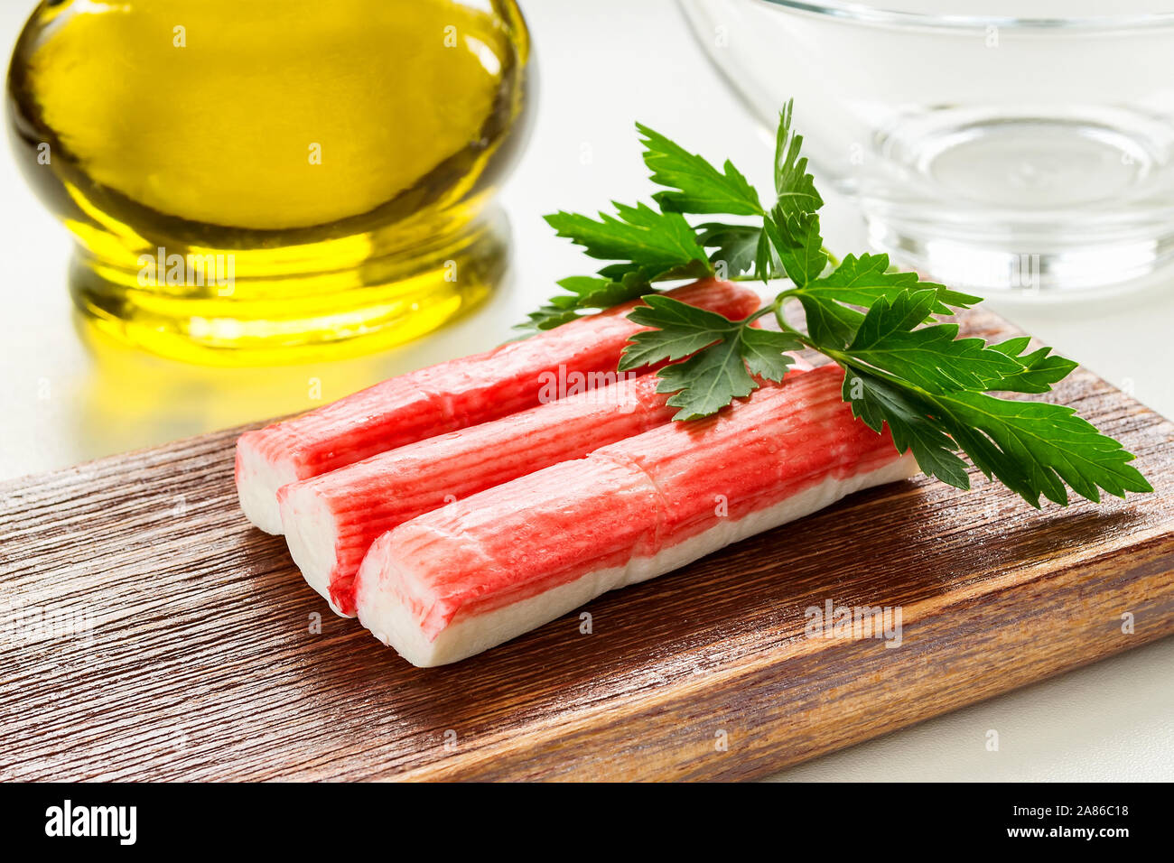 In der Nähe der Zeile von Surimi Crab Sticks auf einer hölzernen Schneidebrett in der Nähe von Olivenöl Glas Glas. Meeresfrüchte und Zutat für Salate. Das gesunde Essen. Stockfoto