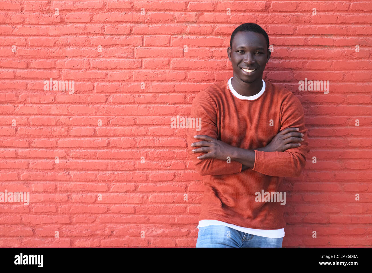 Portrait der Afrikanischen jungen Mann mit Kamera und lächelnd. Kopieren Sie Speicherplatz auf rote Wand im Hintergrund. Stockfoto