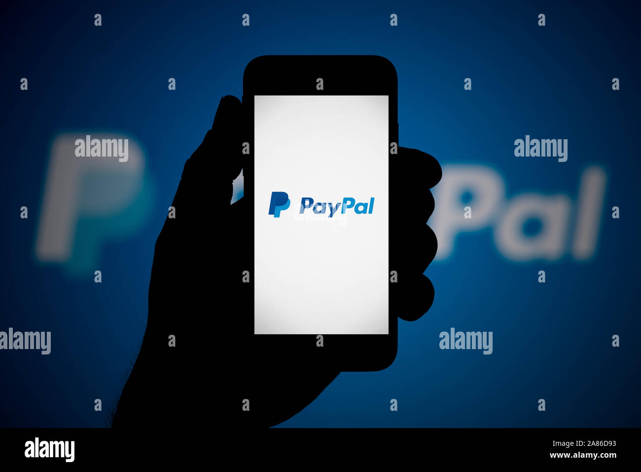 Ein Mann schaut auf seinem iPhone die zeigt das PayPal Logo, mit dem gleichen Logo im Hintergrund (nur redaktionelle Nutzung). Stockfoto