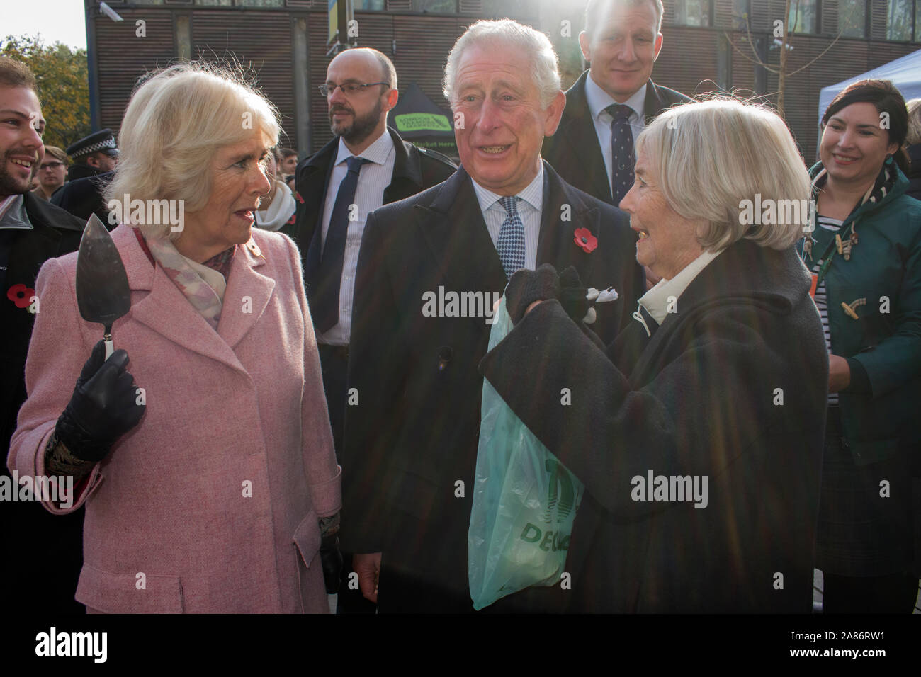 Prinz Charles und Camilla die Herzogin von Cornwall auf dem Schweizer Bauernmarkt, wo sie Stände treffen. Charles hat sich entspannt und lacht, Camilla mit einem Kuchenschneider. Leibwächter stehen hinter ihnen. Es ist der 20. Jahrestag des London Farmers Market. UK 2019. 2010er Jahre HOMER SYKES Stockfoto