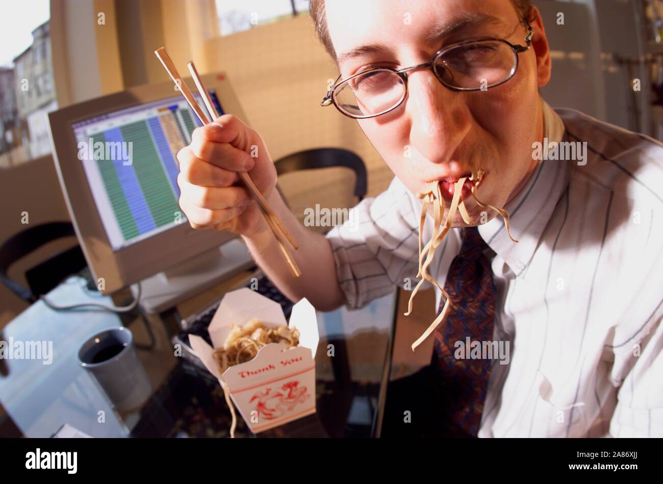 Ein Kaukasier Männlich Büroangestellter sein Gesicht Füllung mit chinesischen Takeout lo mein Stockfoto