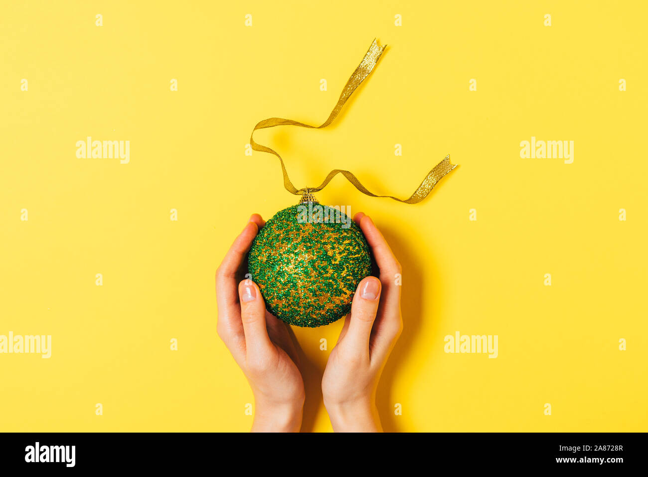 Weibliche Hände halten große Christmas Ball auf gelbem Hintergrund, Ansicht von oben. Stockfoto