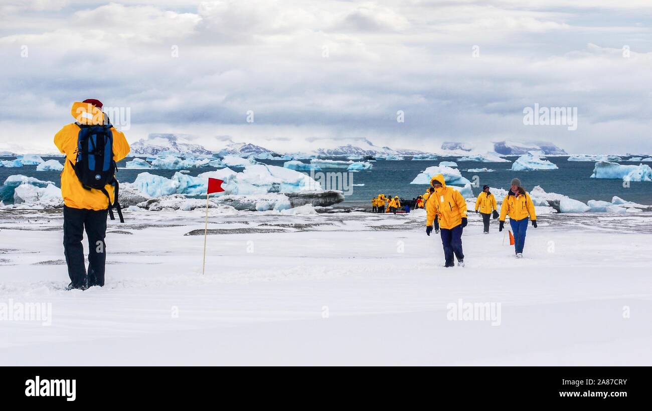 Tourismus in der Antarktis, als Touristen tragen passende parkas Spaziergang über Schnee, mit Blick auf das Meer und die Eisberge im Hintergrund. Stockfoto