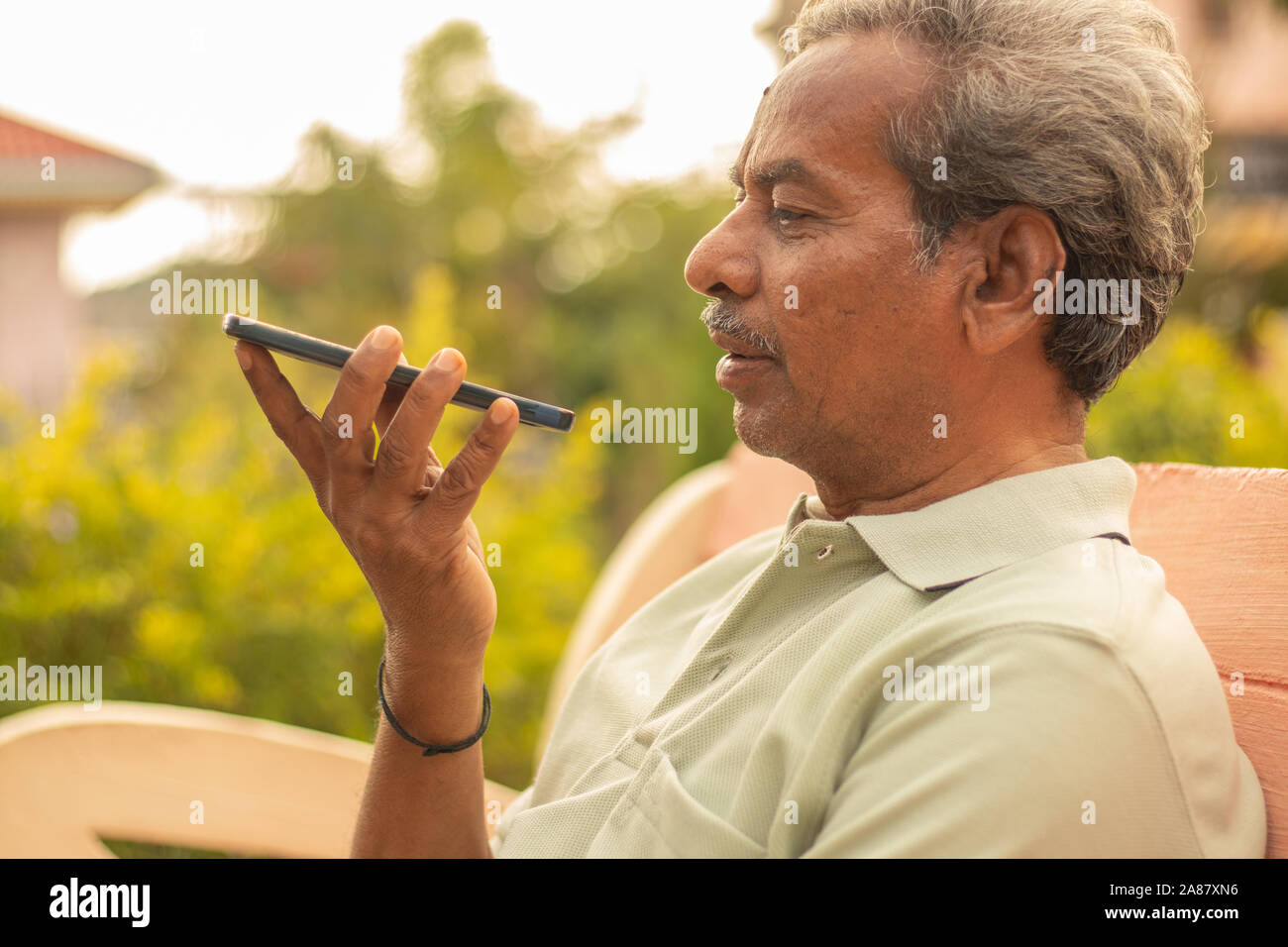 Ältere Menschen mit virtuellen Assistenten in Telefon - Indische ältere Mann mit Voice Command auf dem alten Mann auf dem Smartphone im Freien. Stockfoto