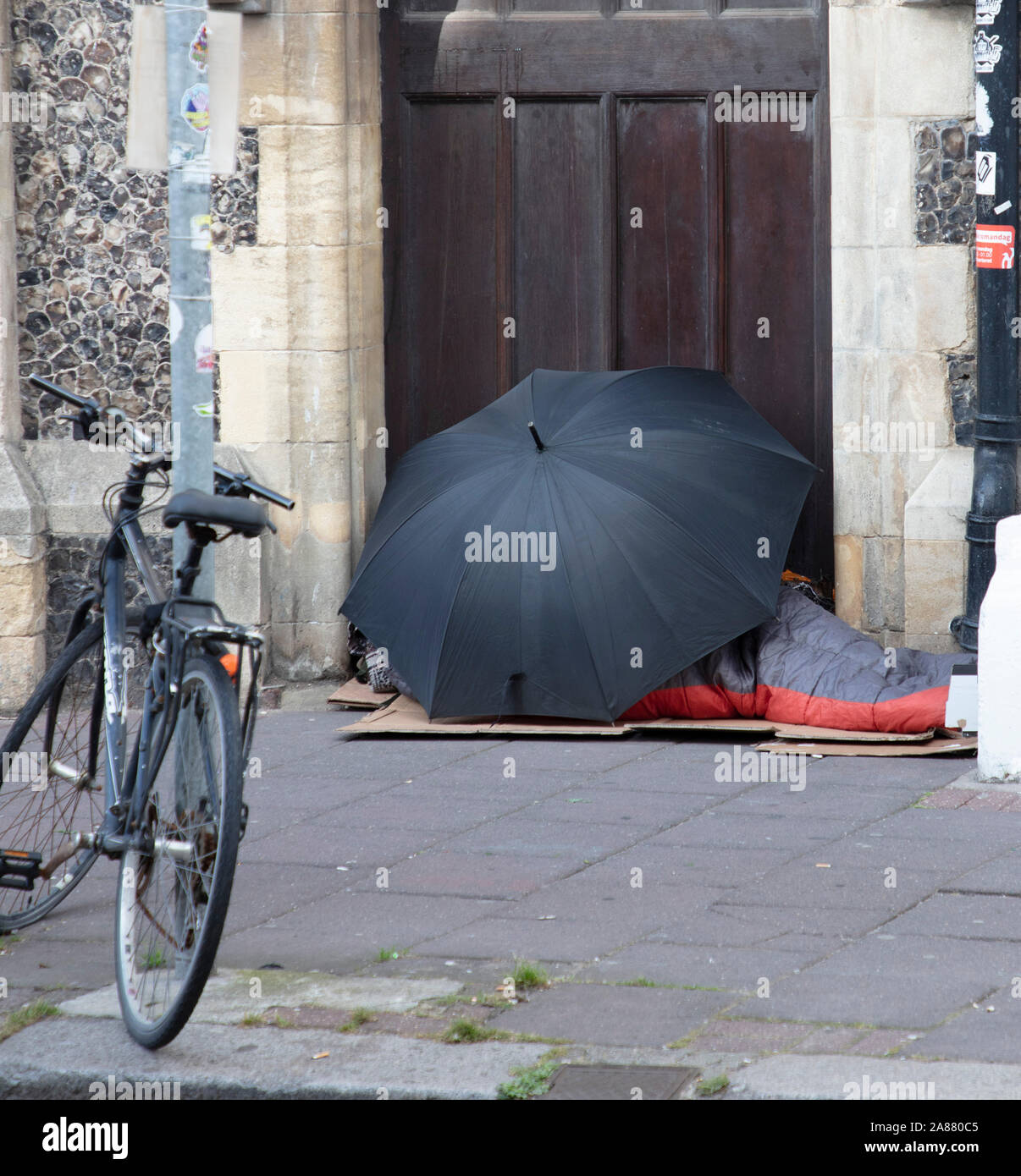 Eine obdachlose Person schlafend in einer Tür unter einem Regenschirm in Brighton, Großbritannien Stockfoto