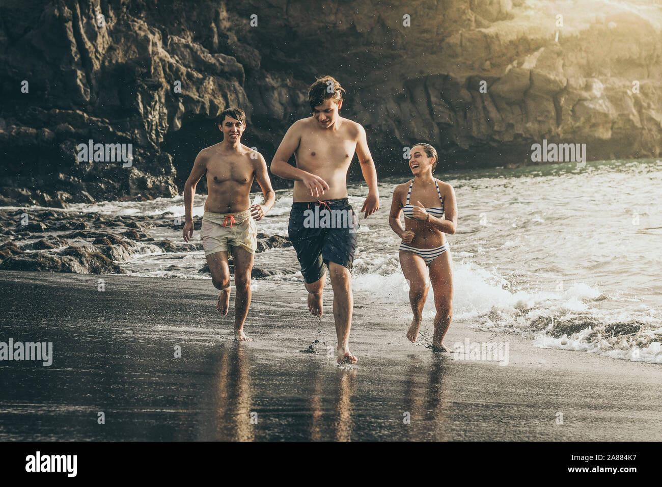 Jugendliche in das Wasser des Meeres bei Sonnenuntergang. Genießen Gruppe von jugendlich mit Pause von der Schule springen glücklich im Meer Menschen Urlaub Spaß Stockfoto