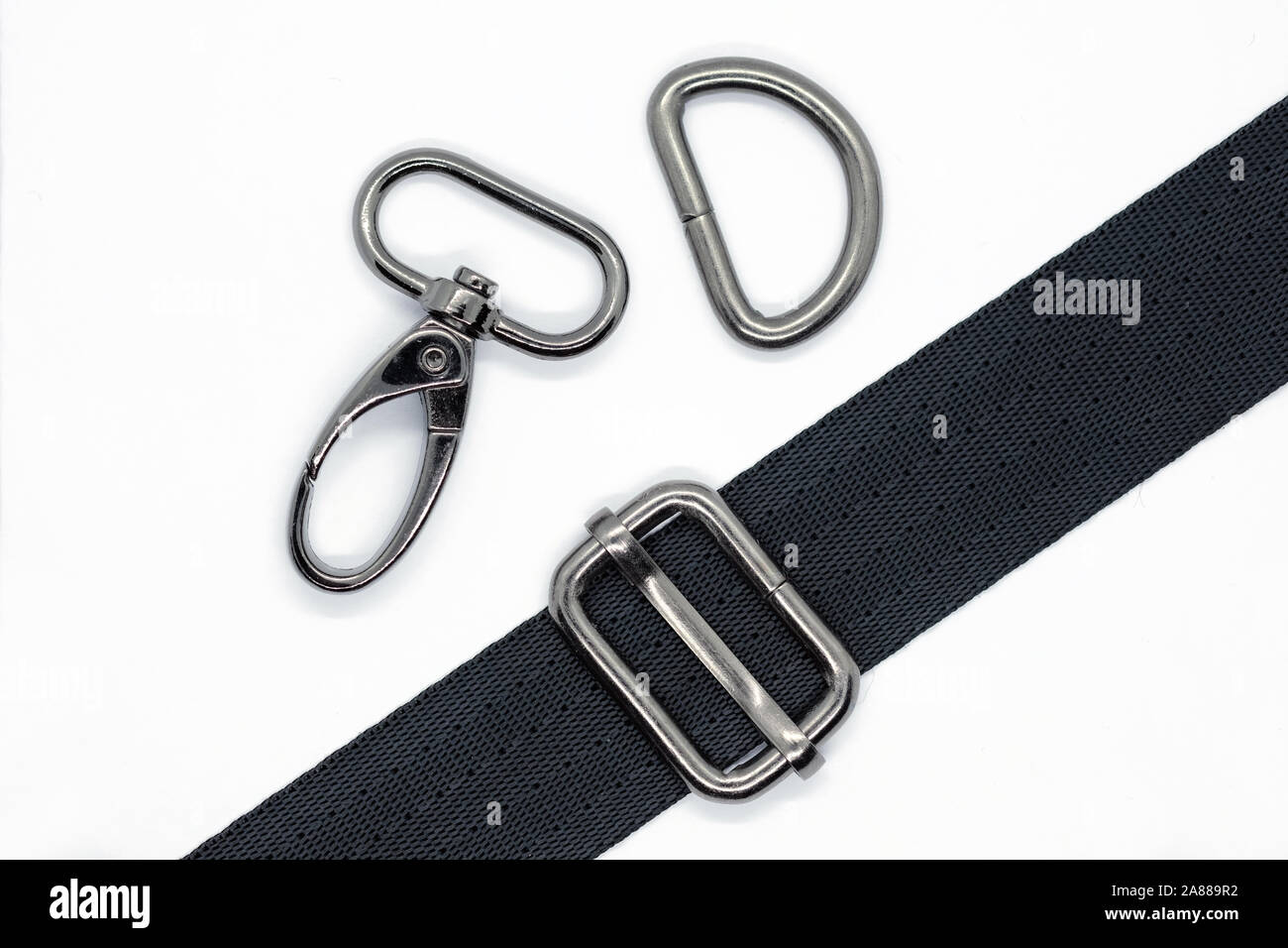 Nähen von Beschlägen für die Herstellung von Taschen und Rucksäcken. Karabiner, halben Ring und Höhenversteller in dunklen Nickel Farbe auf weißem Hintergrund. Schwarzes Band für Stockfoto