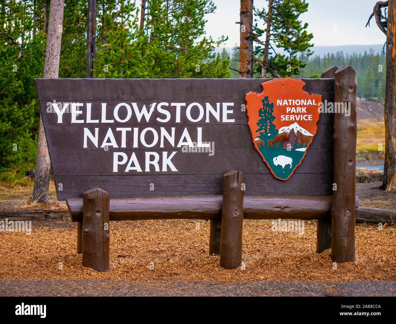 Der Yellowstone National Park Holz- Eingang unterzeichnen, mit der gefallenen Blätter im Herbst unter und Wald Bäume im Hintergrund. Stockfoto