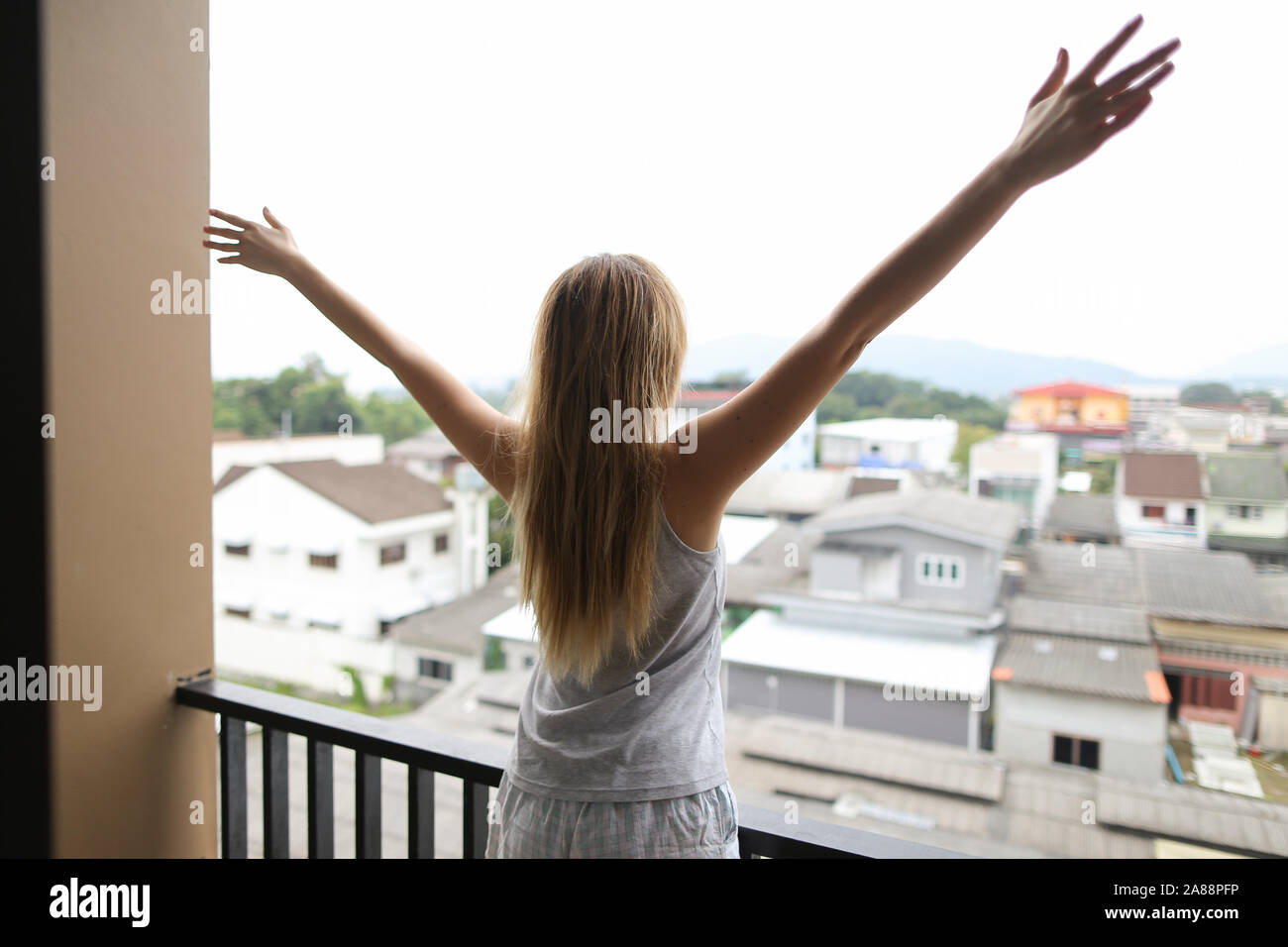 Junge kaukasier Frau Sommer Schlafanzug stehen auf Balkon und suchen bei Gebäuden mit erhobenen Händen. Stockfoto