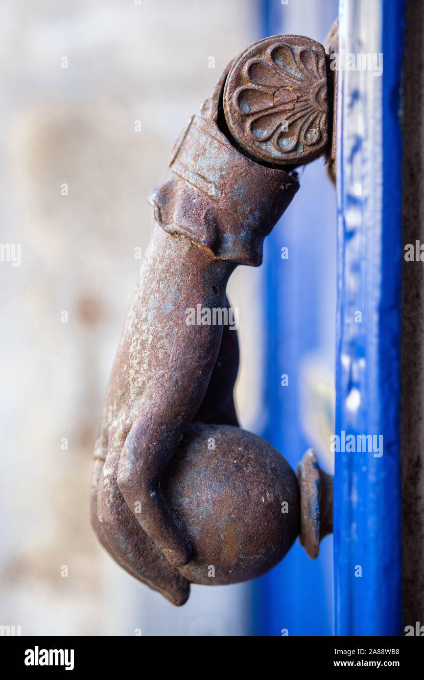 Türklopfer aus Metall, die eine Hand mit einem Schüssel auf eine blaue Tür Stockfoto
