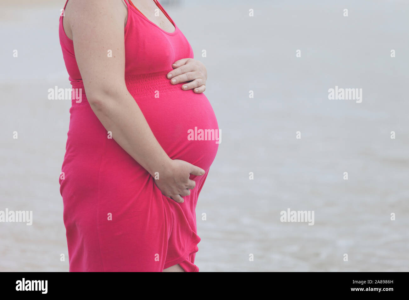 Schwangere Frau trägt rosa Kleid am Strand Stockfoto