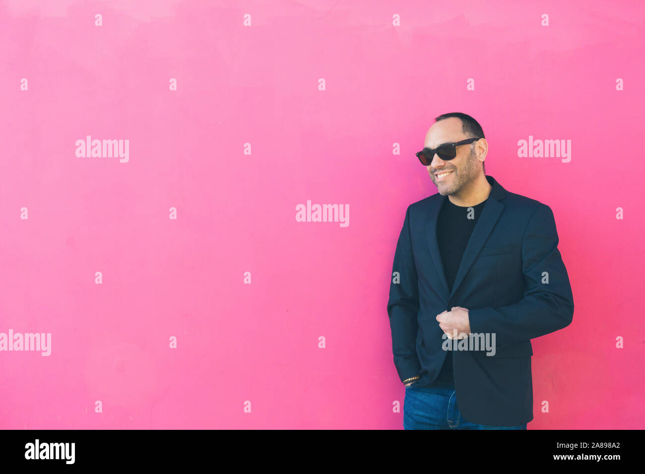 Lächelnder Mann mit Sonnenbrille und Blazer an pinker Wand Stockfoto