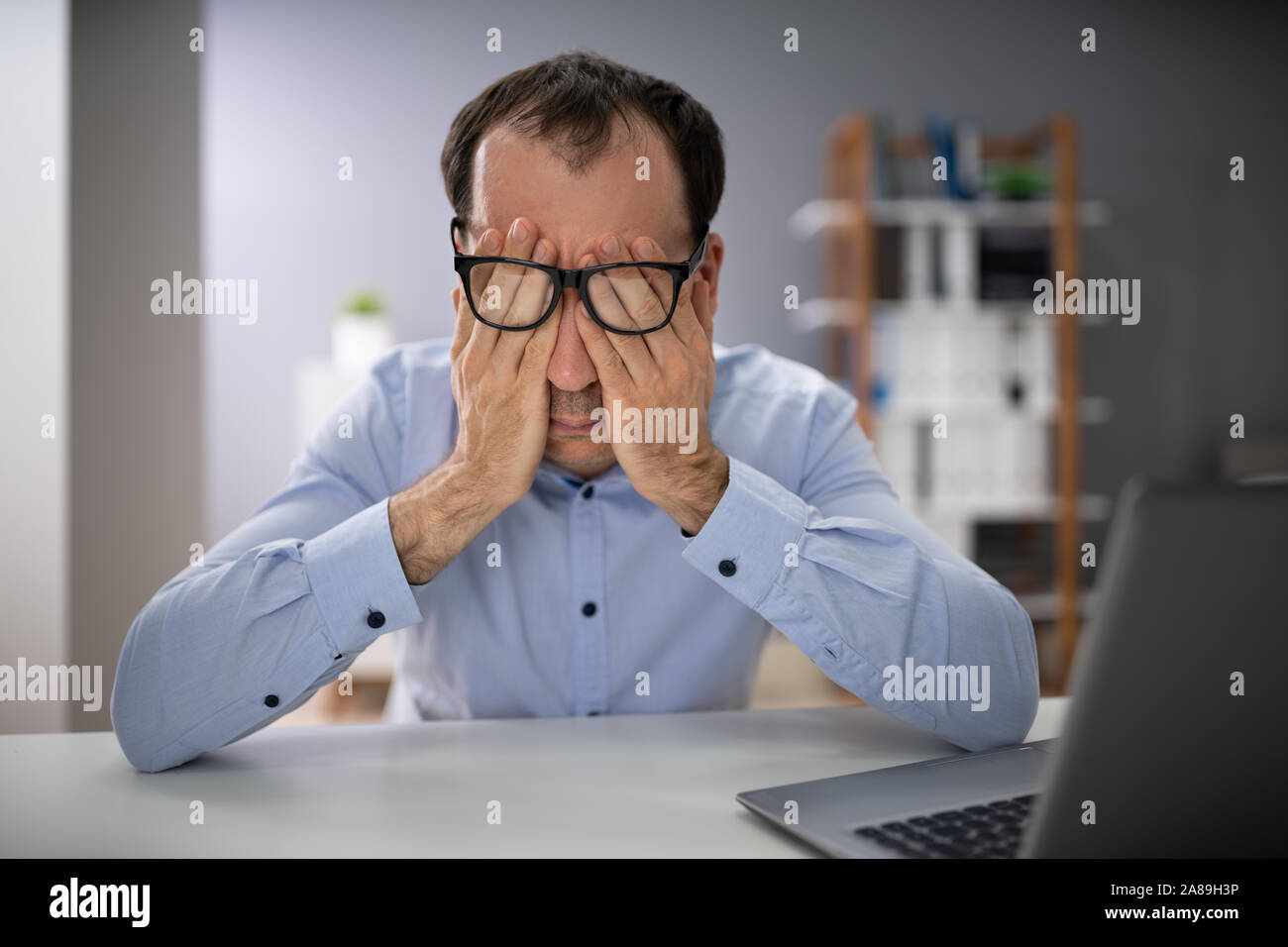 Der Mann mit der Hand über das Gesicht mit Brille im Büro Stockfoto