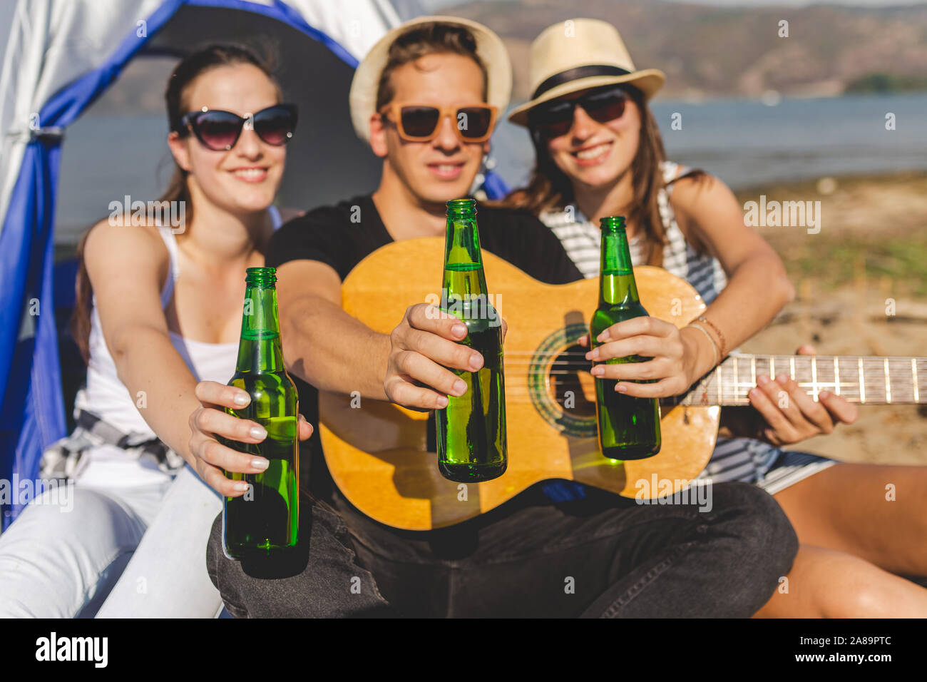 Guitar Player mit seinen Freunden zeigen Flaschen Bier, während eine tolle Zeit in beim Camping am Strand. Stockfoto
