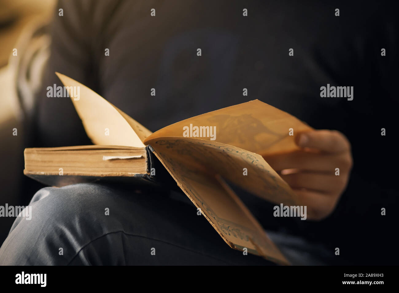 Ein Mann in der dunklen Kleidung und Jeans sitzt und hält in den Händen der offenen alten Buch, beabsichtigt, zu lesen. Stockfoto