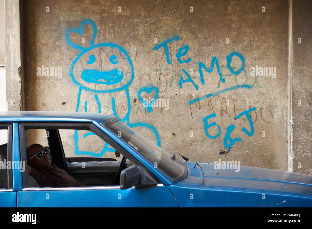 Havanna - 17. MAI 2011: eine Kubanische Mann sitzt in blau Auto neben einer Wand mit Graffiti in Spanisch, die besagt, dass te amo (ich liebe Dich). Stockfoto