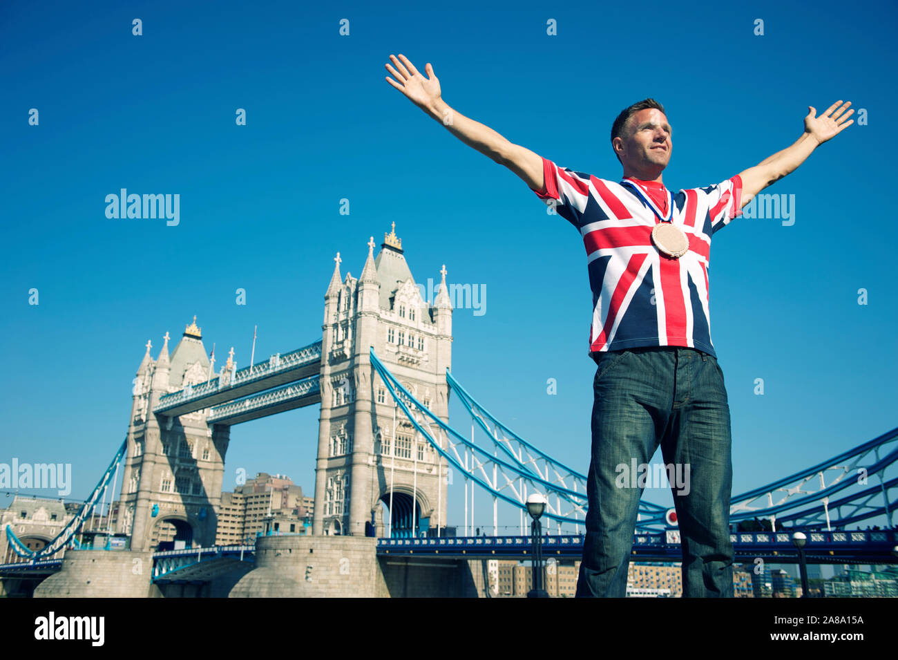 Patriotische junge britische Mann in einem Union Jack T-Shirt mit Goldmedaille vor der Tower Bridge London Stockfoto