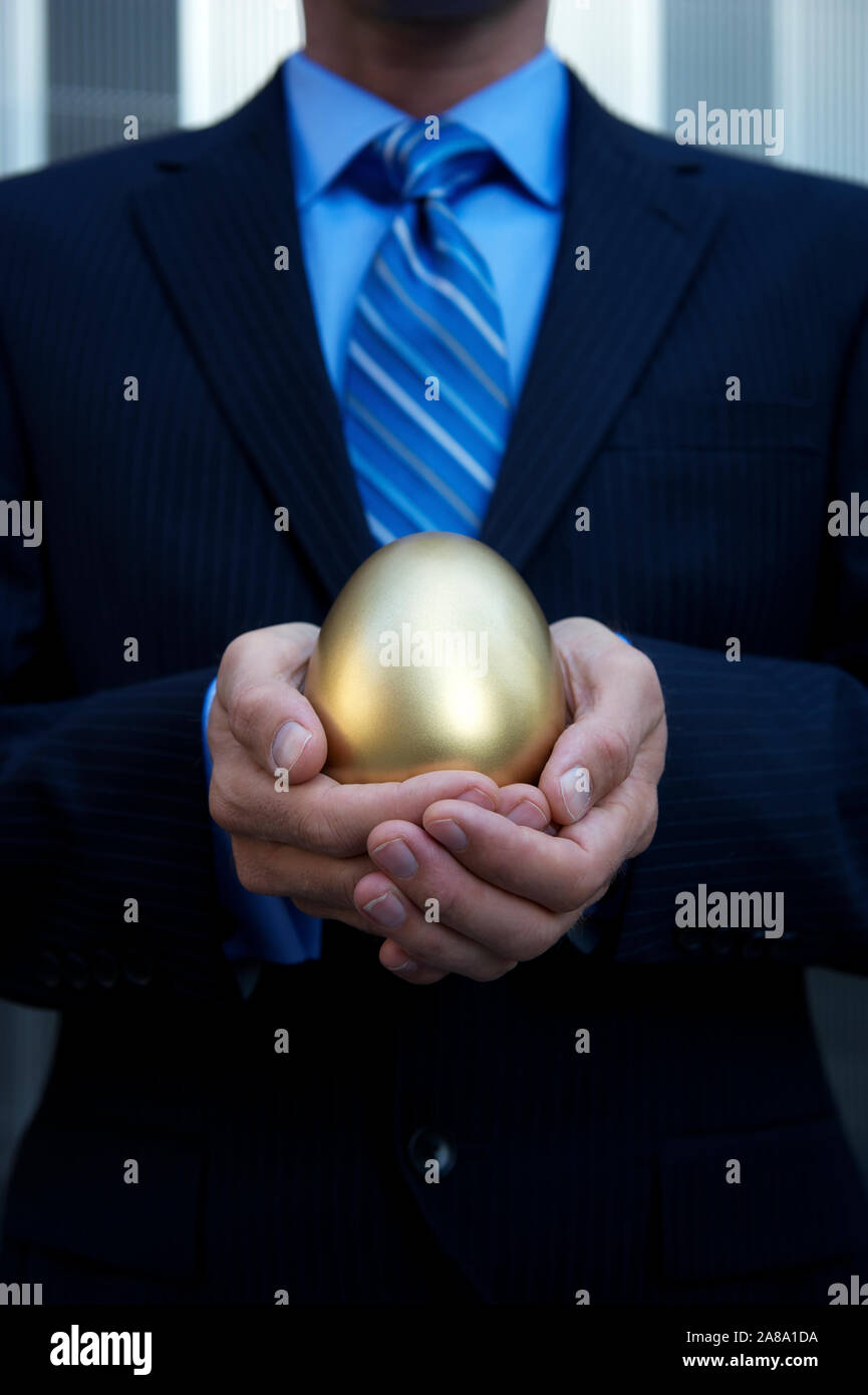 Nicht erkennbare Geschäftsmann mit einem goldenen Ei in seinen Händen stehen draußen in einen dunklen Anzug vor einem modernen Business Hintergrund in Halterung Stockfoto