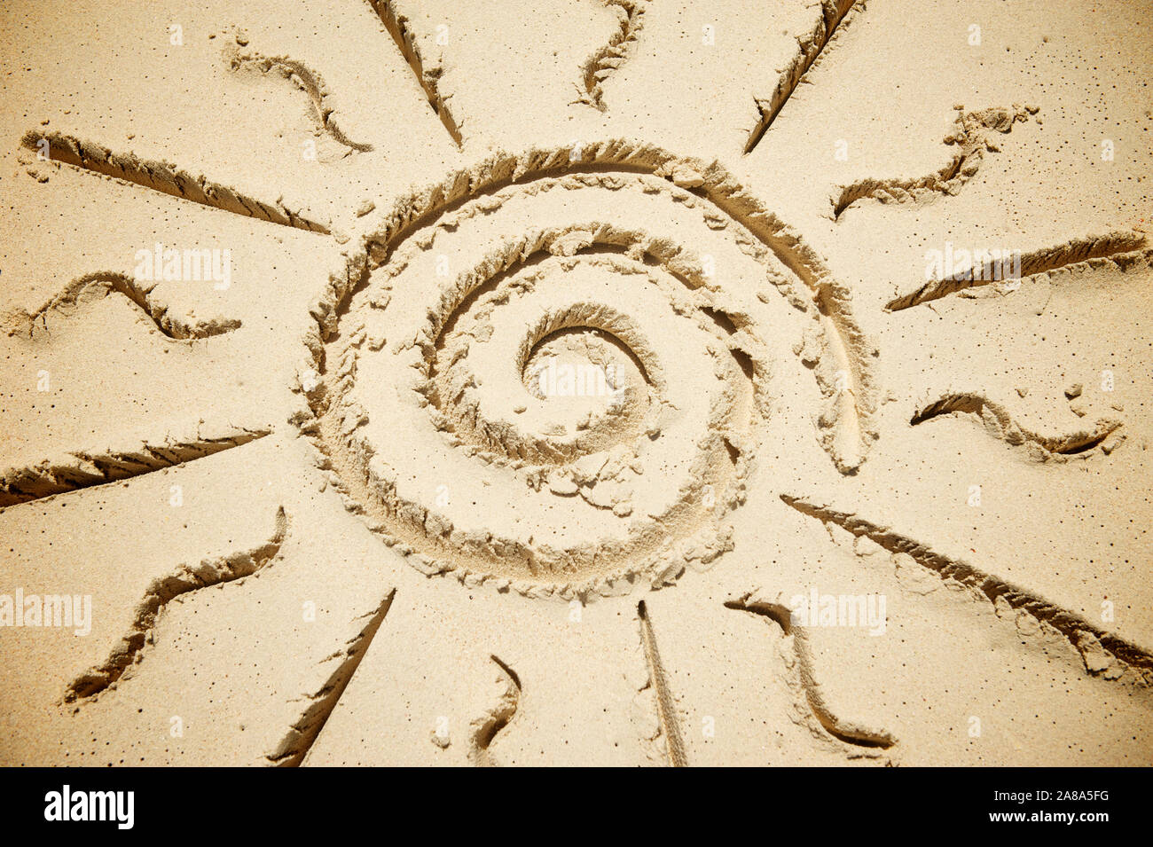 Stilisierten Spirale Sonne mit Strahlen auf eine weiche Sand an einem sonnigen Strand gezeichnet Stockfoto