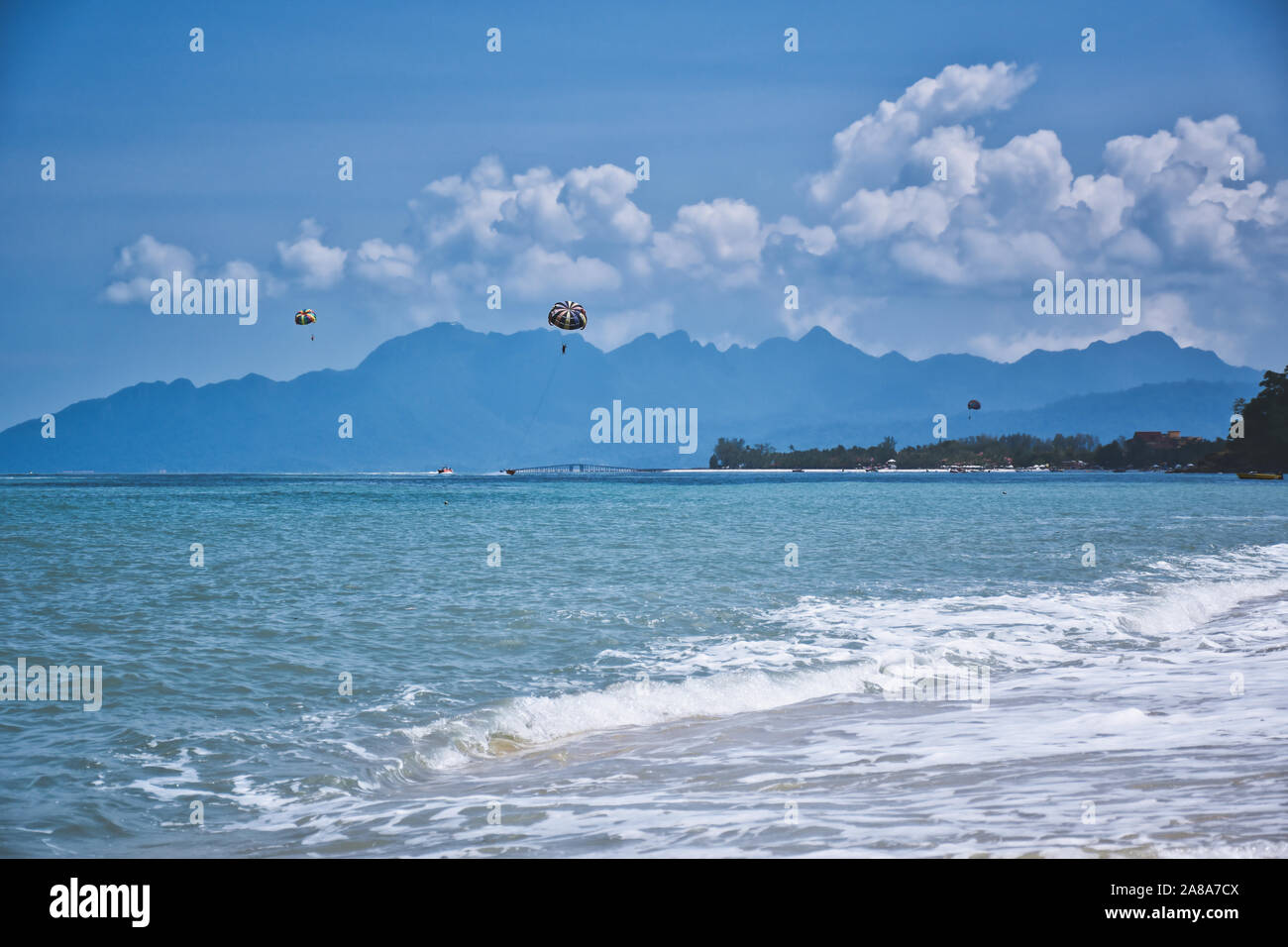 Parasailing auf den Wellen der azurblaue Andamanensee unter dem blauen Himmel in der Nähe der Ufer des wunderschönen exotischen Sandstrand und eine atemberaubende Cenang Beach in Langka Stockfoto