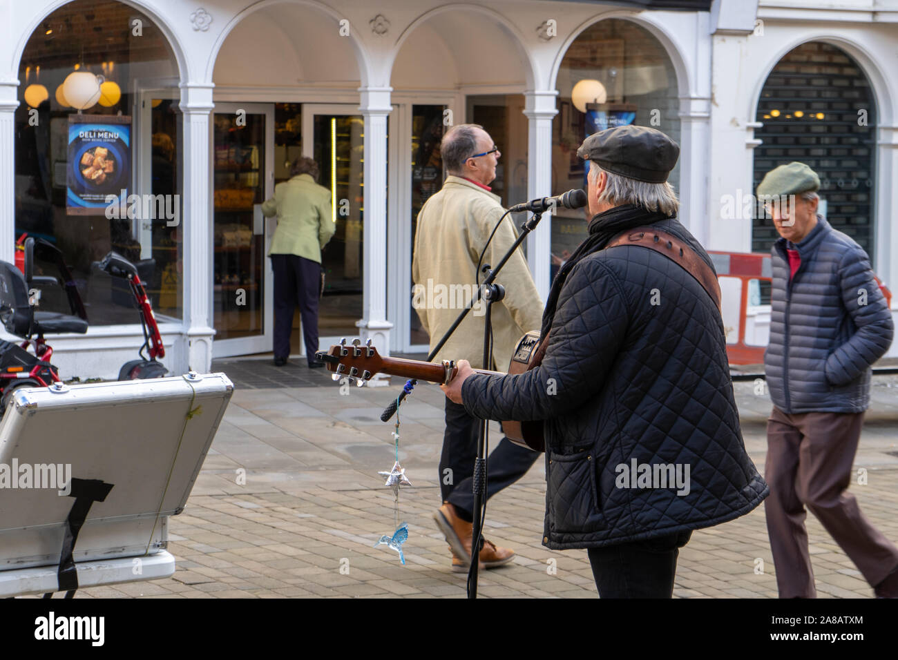 Ein im mittleren Alter straßenmusikant Unterzeichnung an Mikrofon und Gitarre spielen mit Käufern vorbei Stockfoto