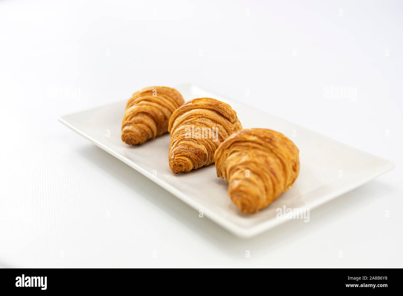 Seitenansicht von drei köstliche, frisch gebackene Croissants und auf einem weißen Teller auf weißem Hintergrund Stockfoto