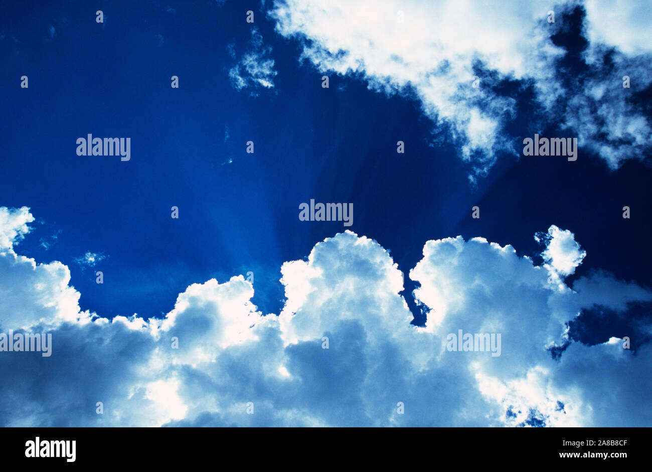 Sonnenstrahlen glänzenden hinter weißen Wolken im blauen Himmel Stockfoto