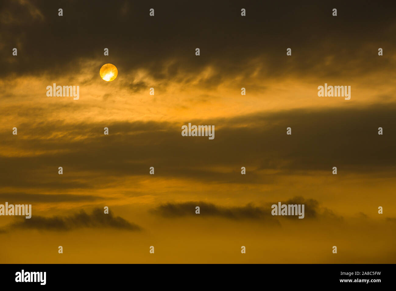 Dramatischer orangefarbener, unheimlicher Himmel und die Sonne, die teilweise durch das Wolkentuch bedeckt ist, Singapur. Stockfoto