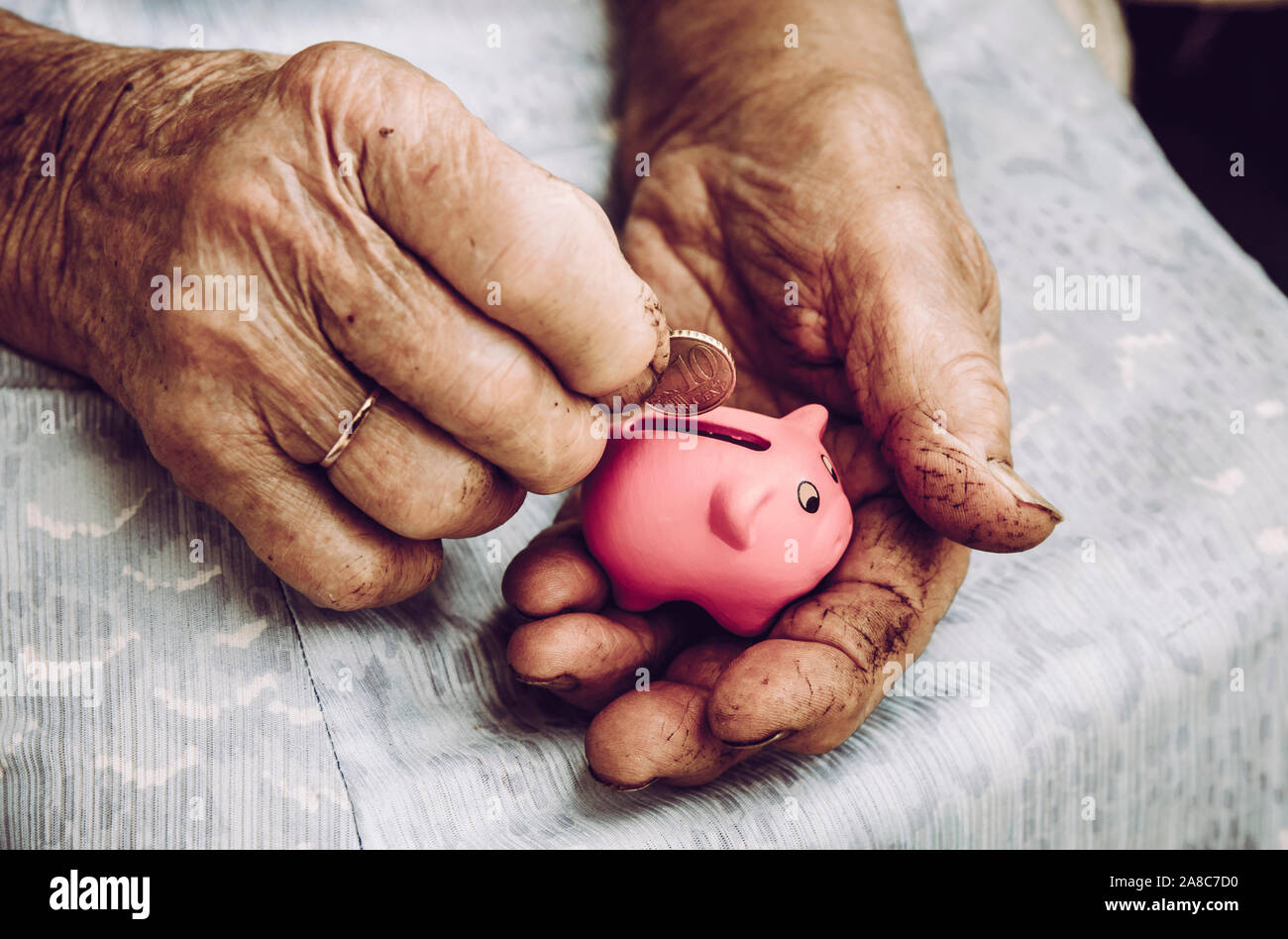 Nahaufnahme der alten schmutzigen, rauen älteren älteren, pensionierten Frauen, die die winzige pinkfarbene Schweinebank halten. Kleines Rentenkonzept. Stockfoto